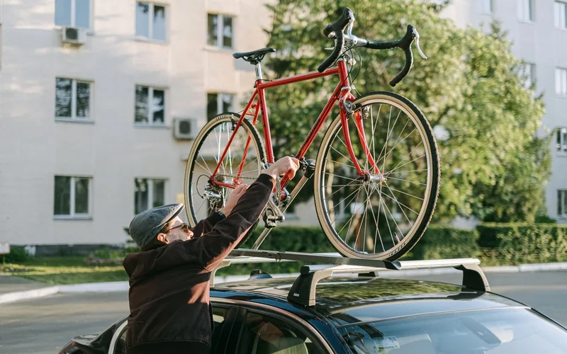 Man tilt een fiets op de dwarsdragers op het dak van zijn auto