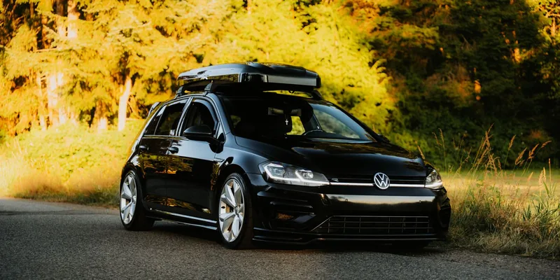 Zwarte Volkswagen Golf met zilvergrijze dakkoffer op dakdragers langs een zonnige bosweg