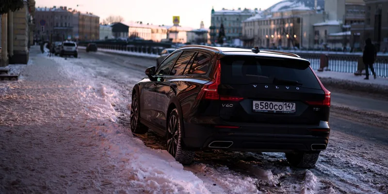 Zwarte Volvo V60 stationwagen met dakrails op een besneeuwde stadsstraat