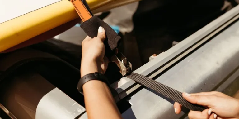 Handen die een spanband vastzetten over de dakdrager van een auto