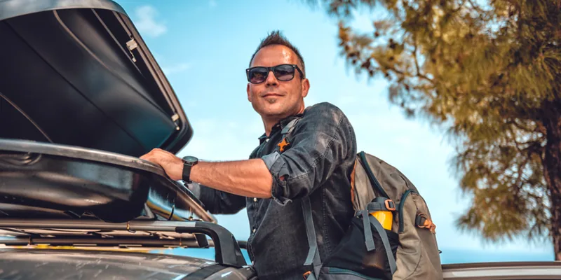 Man met rugzak sluit de dakkoffer op het dak van zijn auto