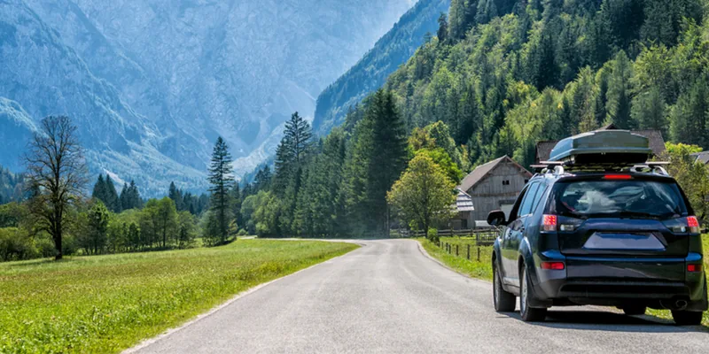 Donkere SUV met dakkoffer op een bergweg met uitzicht op de Alpen