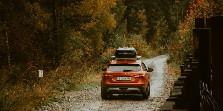 Oranje cross-over met dakkoffer op de dakdragers op een bospad in de herfst
