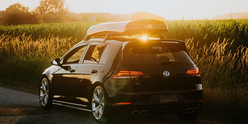 Auto met grijze dakkoffer op dakdragers op een landweg bij zonsondergang