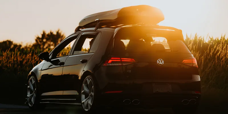 Grijze dakkoffer op de dakdragers van een zwarte hatchback bij zonsondergang