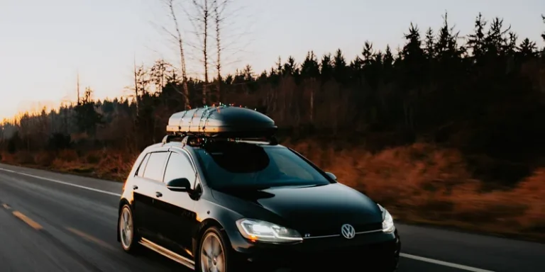 Grote dakkoffer op de dakdragers van een zwarte auto die bij zonsondergang over een bosweg rijdt