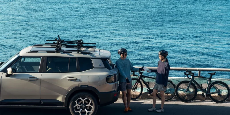 SUV met fietsdragers op de dakdragers langs het water, fietsers ernaast