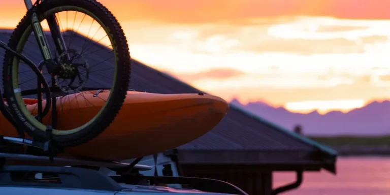 Kajak en mountainbike op de dakdragers van een auto bij zonsondergang