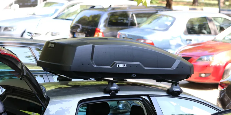 Zwarte Thule dakkoffer op de dakdragers van een auto op een parkeerplaats