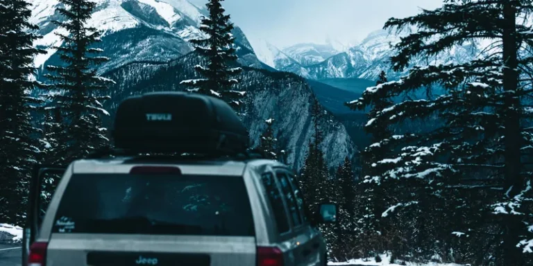 SUV met Thule dakkoffer op een besneeuwde bergweg tussen de dennenbomen