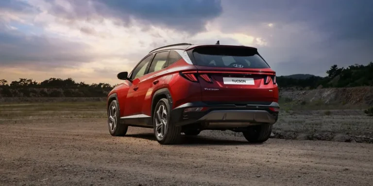 Rode Hyundai Tucson met dakrails op een onverharde weg in de schemering