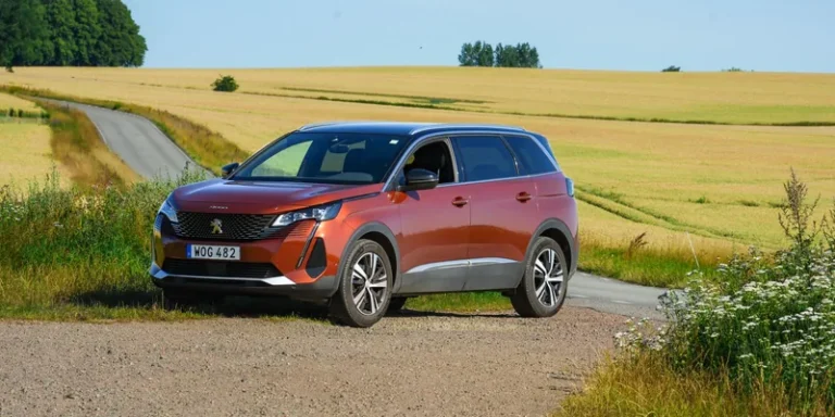 Oranje Peugeot SUV op een landweg tussen graanvelden