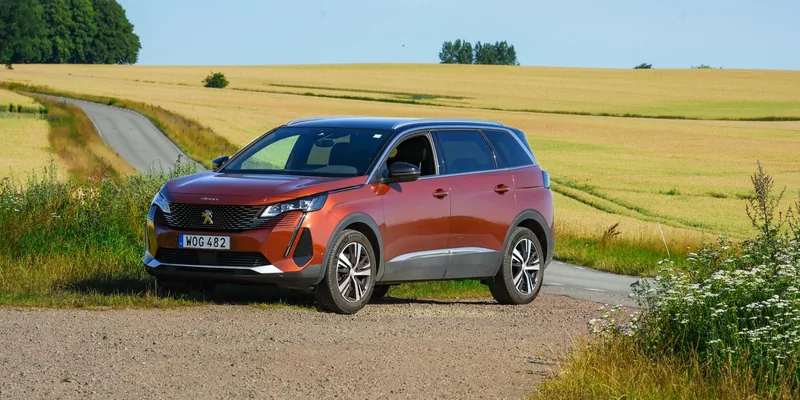 Oranje Peugeot SUV op een landweg tussen graanvelden