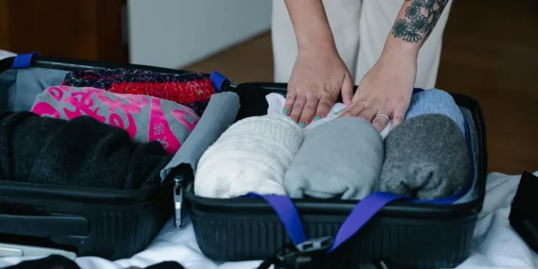 Handen pakken opgerolde kleding in een geopende reistas